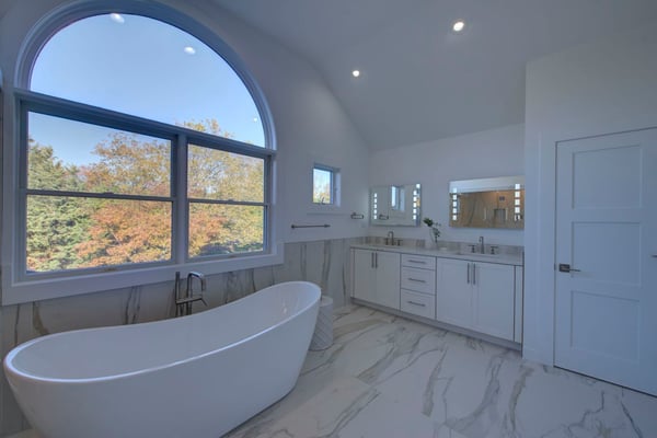 Large window over soaking tub in a white marble bathroom