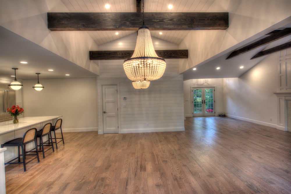 Livingroom with shiplap accent wall white beaded chandelier and kitchen to the left has brown hardwood floors.pdf_1